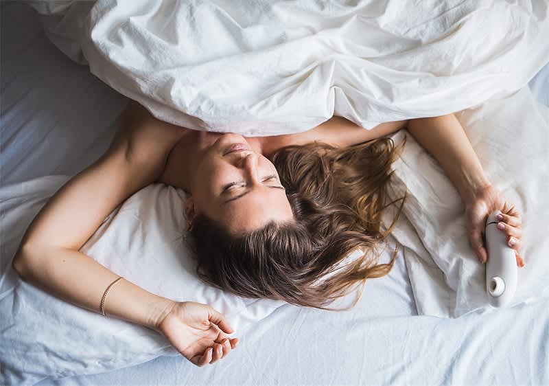 Frau im Bett mit weißer Bettwäsche und einem Vibrator in der Hand