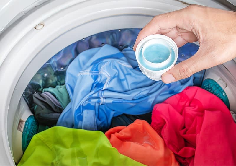 Waschmaschine mit bunter Kleidung und Hand hält Waschmittelkapsel