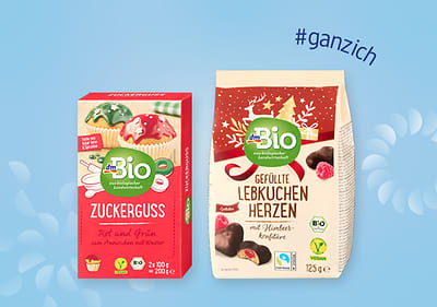 Zwei Produktverpackungen von dmBio: links Zuckerstreusel in Rot und Grün, rechts gefüllte Lebkuchenherzen mit Schokoladenüberzug. Text „#ganzich“ oben rechts