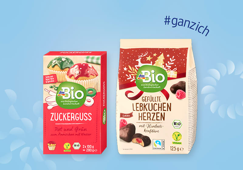 Zwei Produktverpackungen von dmBio: links Zuckerstreusel in Rot und Grün, rechts gefüllte Lebkuchenherzen mit Schokoladenüberzug. Text „#ganzich“ oben rechts
