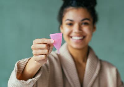 Junge Frau mit Menstruationstasse und Binde in der Hand 