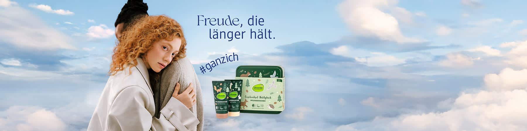Eine Frau mit lockigem Haar umarmt eine Person, daneben Alverde-Pflegeprodukte und der Text „Freude, die länger hält. #ganzich“