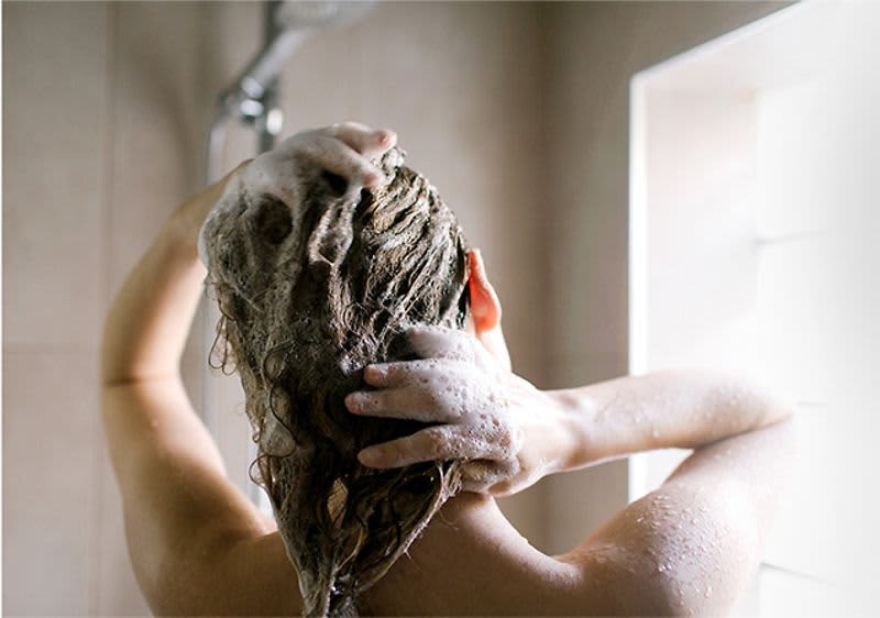 Frau beim Haarewaschen unter der Dusche mit Shampoo und Schaum