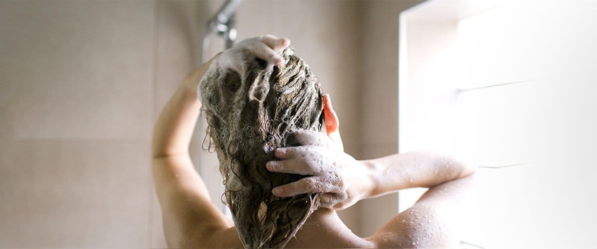 Frau beim Haarewaschen unter der Dusche mit Shampoo und Schaum