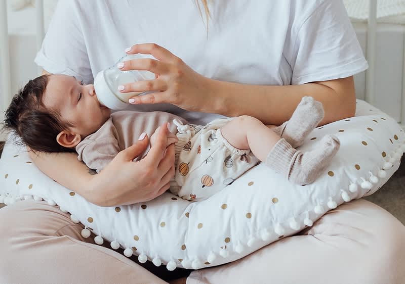 Baby bekommt Flaeschchen im Arm der Mutter