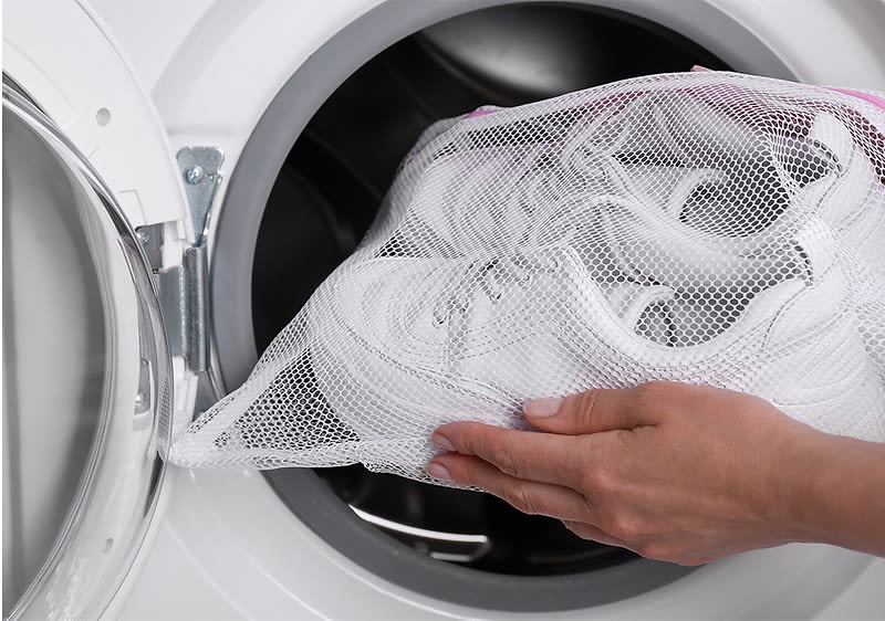 Frau die Schuhe in die Waschmaschine gibt