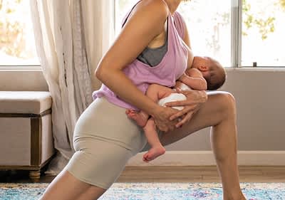 Frau macht Dehnübung mit Baby im Arm