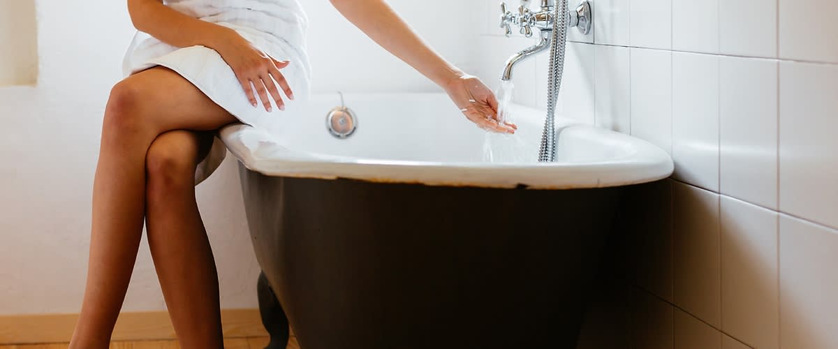Frau auf Rand einer Badewanne mit fließendem Wasser aus Wasserhahn