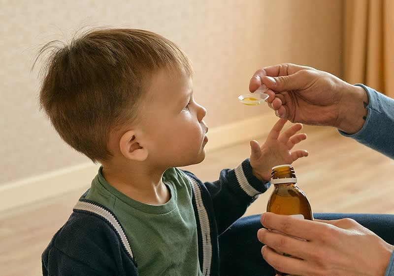 Mama gibt Sohn Medikament auf Loeffel