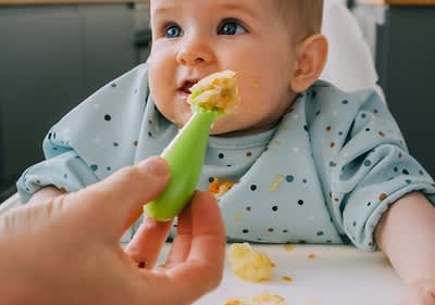 Baby in Hochstuhl wird mit einem Löffel brei gefüttert