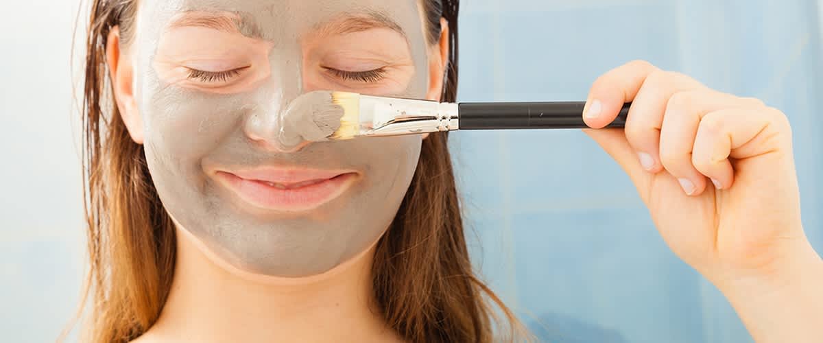 Frau trägt sich mit Pinsel eine Gesichtsmaske aus Tonerde auf