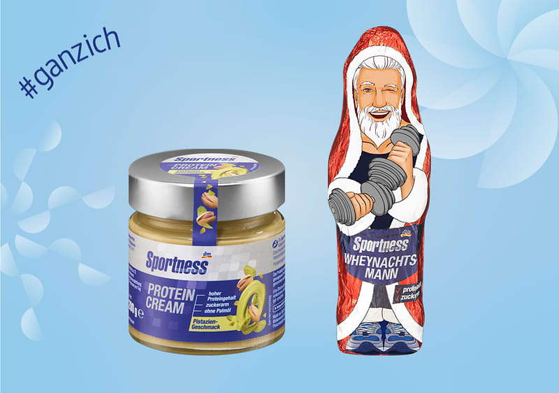 Links ein Glas mit der Aufschrift „Sportness Protein Cream“ und Bananenmotiv, rechts eine Figur in rotem Mantel mit Hanteln, daneben der Text „#ganzich“