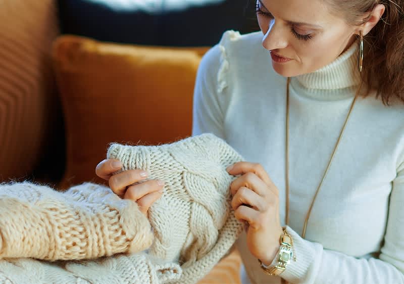 Frau mit Pulli in der Hand auf Couch