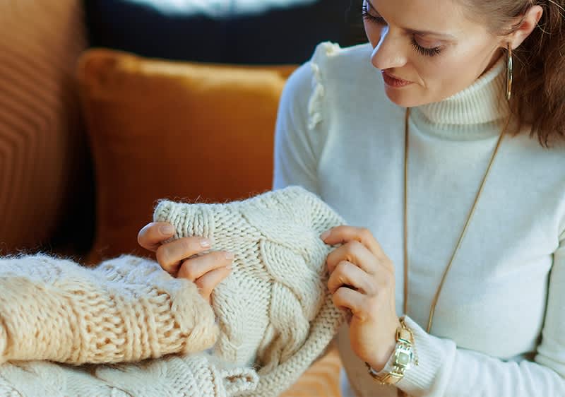 Frau mit Pulli in der Hand auf Couch