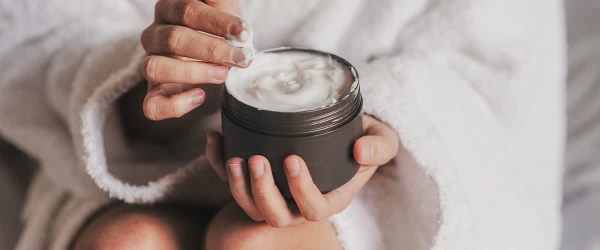 Frau in Bademantel mit Cremedose in der Hand