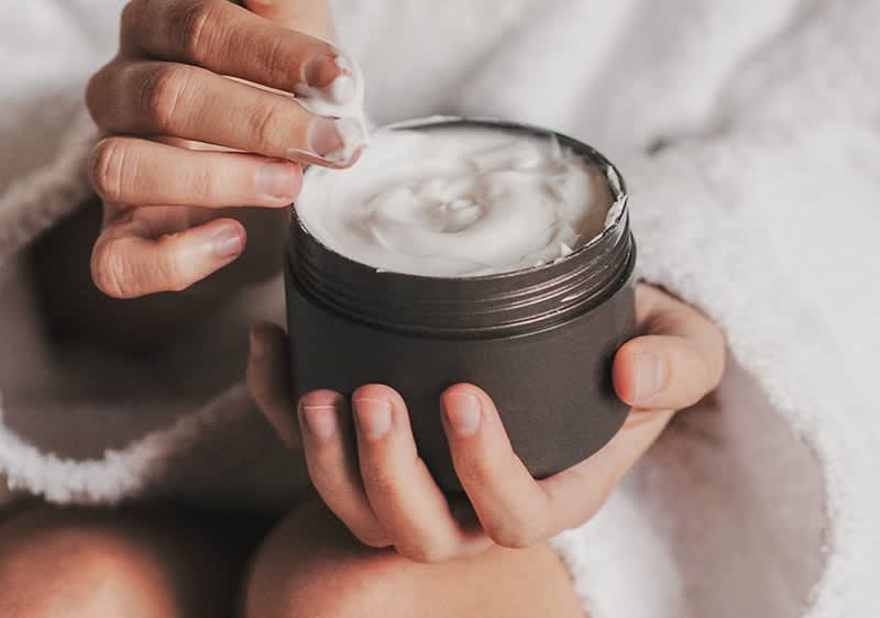 Frau in Bademantel mit Cremedose in der Hand