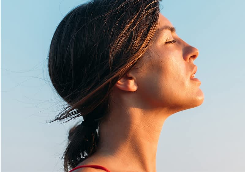 Frau mit geschlossenen Augen schaut zur Sonne rauf