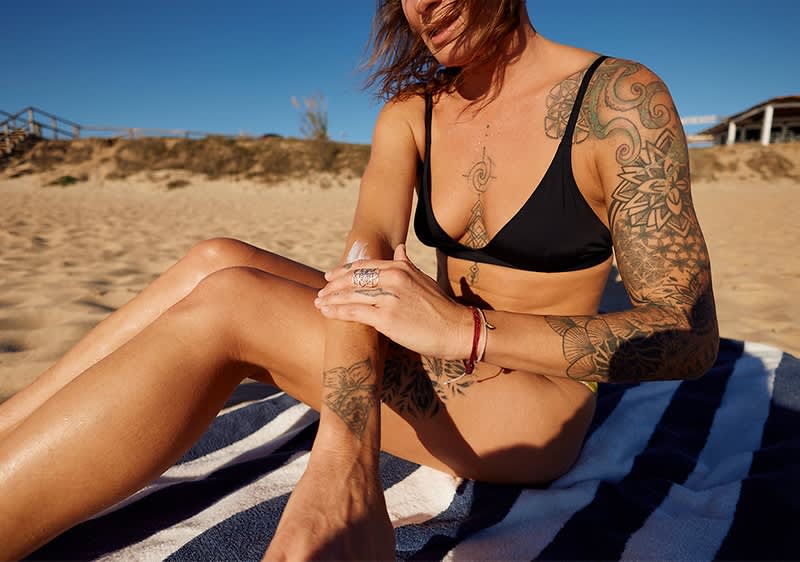 Frau mit Tattoos am Strand beim Sonnen