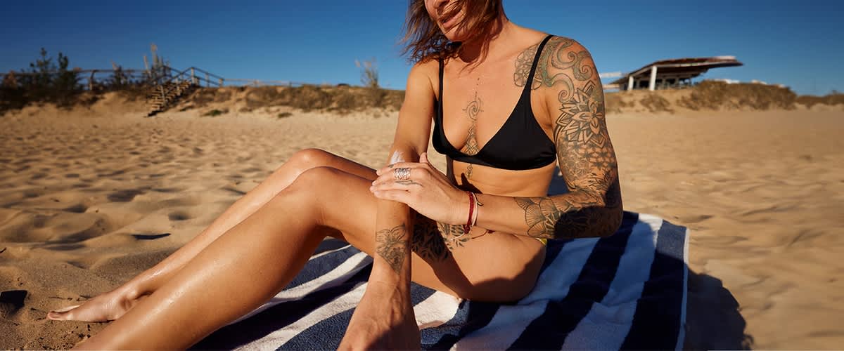 Frau mit Tattoos am Strand beim Sonnen