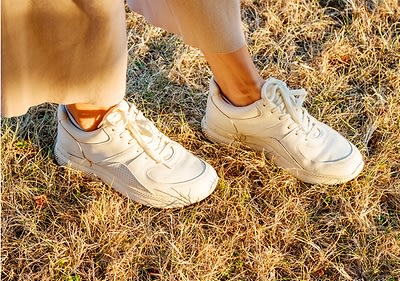 Frauenfüße mit weißen Sneakern auf Wiese