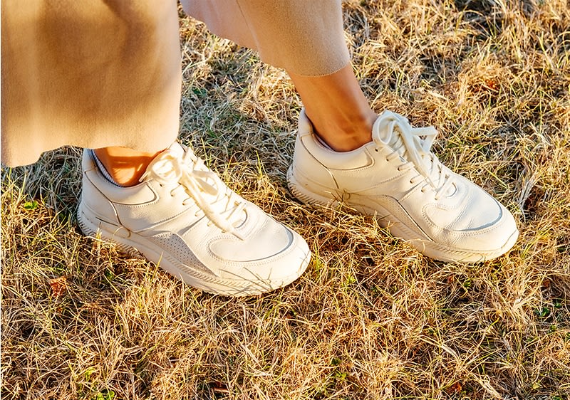 Frauenfüße mit weißen Sneakern auf Wiese