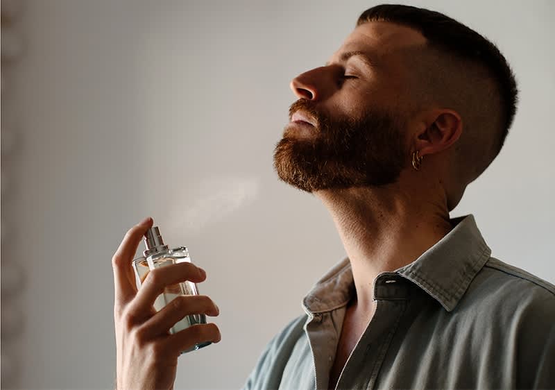 Mann bersprueht sich mit Parfum