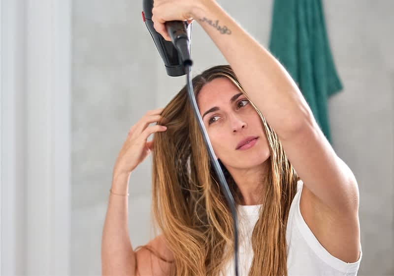 Frau mit langen braunen Haaren beim Foehnen