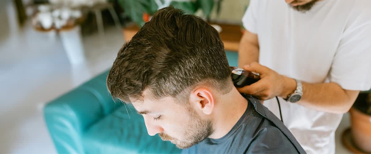 Ein Mann bekommt ein Haarschnitt mit Haarschneidemaschine im Friseursalon