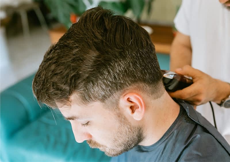 Ein Mann bekommt ein Haarschnitt mit Haarschneidemaschine im Friseursalon