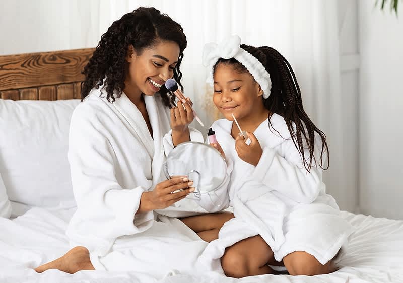 Mutter und Tochter in Bademänteln beim Schminken auf dem Bett