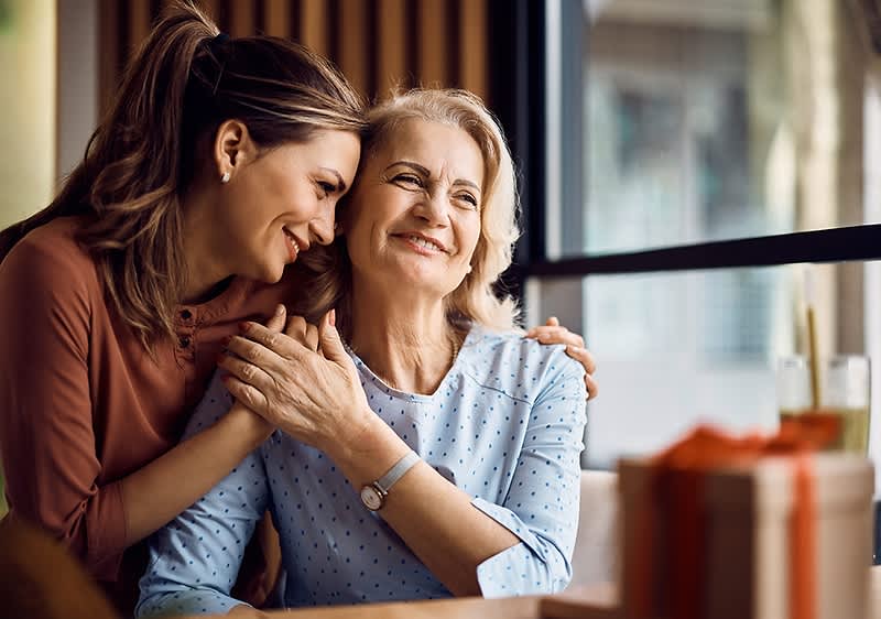 Zwei Frauen umarmen sich in einem Café mit Geschenken auf dem Tisch