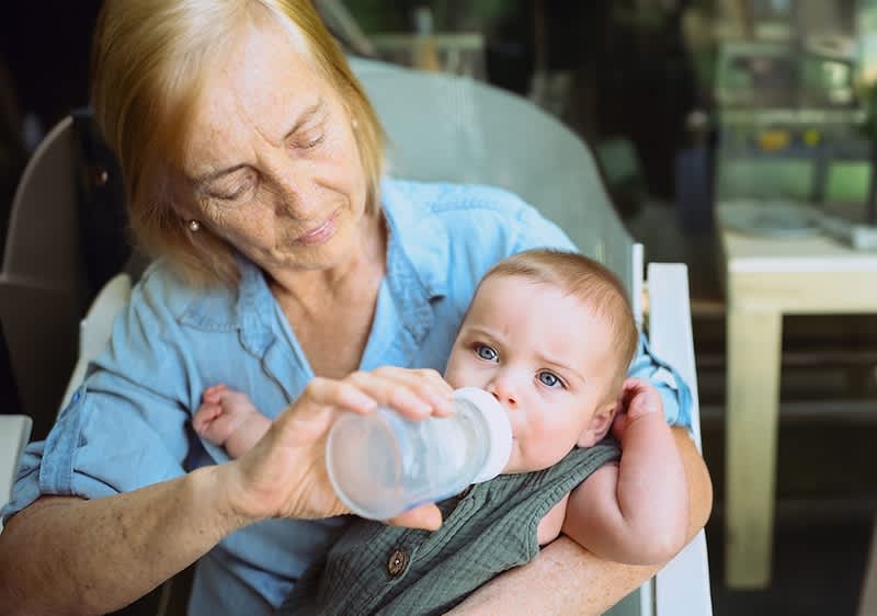 Oma füttert Baby mit Flasche im Restaurant