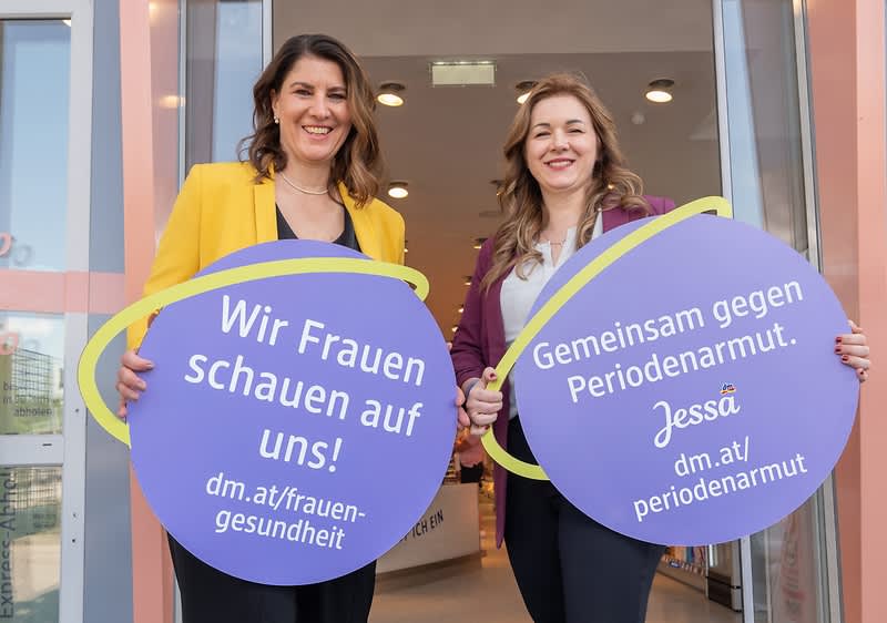 Frauen halten Schilder gegen Periodenarmut vor einem Geschäft