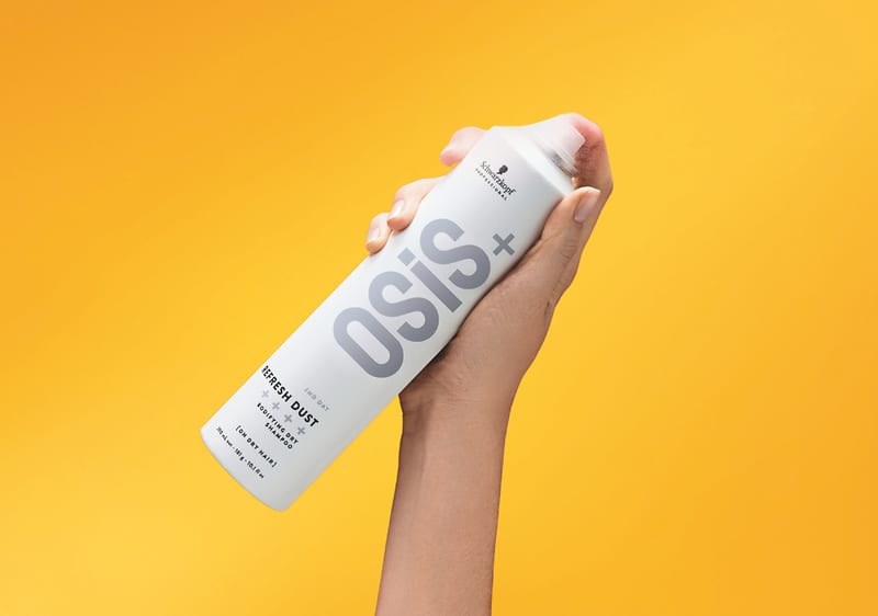 Haarsprayflasche in Hand vor gelbem Hintergrund
