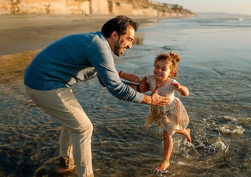 Vater und Tochter spielen am Strand im Wasser