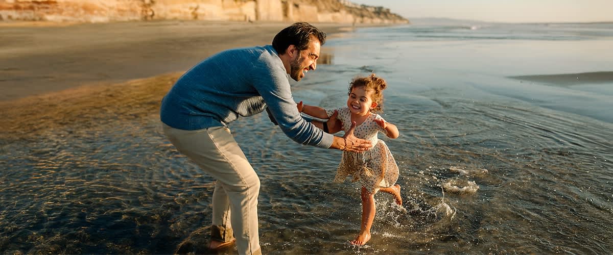 Vater und Tochter spielen am Strand im Wasser