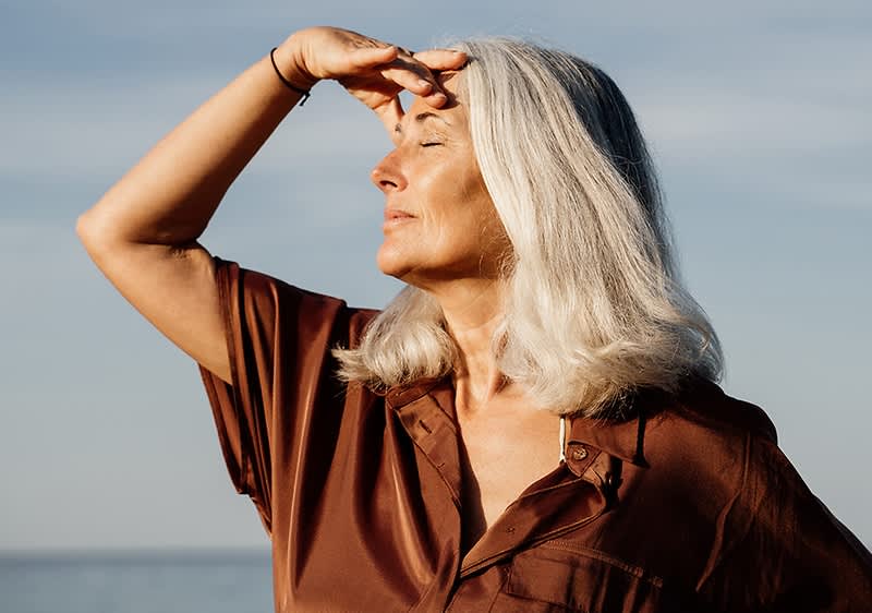 Frau mit grauem Haar in brauner Bluse am Meer