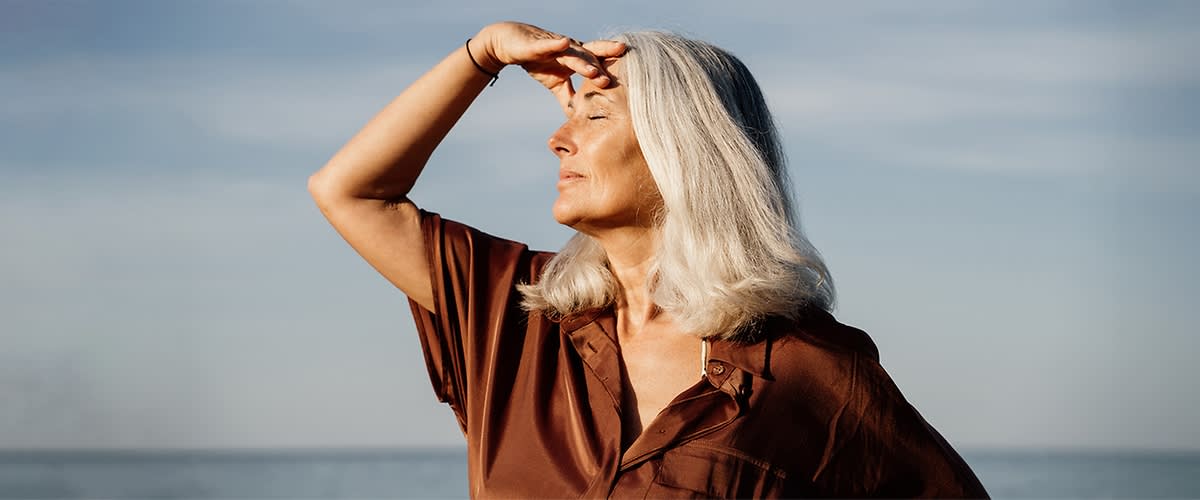 Frau mit grauem Haar in brauner Bluse am Meer