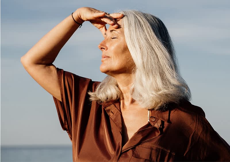 Frau mit grauem Haar am Meer im Sonnenlicht