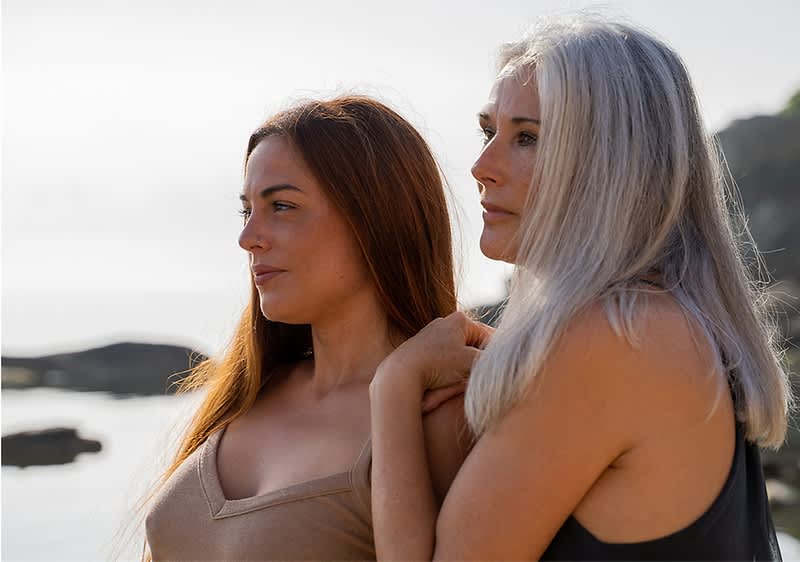 Zwei Frauen am Strand mit Meer und Felsen im Hintergrund