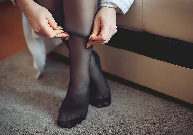 Frau zieht schwarze Strumpfhose an während sie auf einem Sofa sitzt