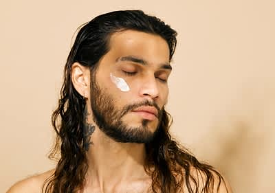 Mann mit nassen Haaren und tätowiertem Hals vor beigem Hintergrund