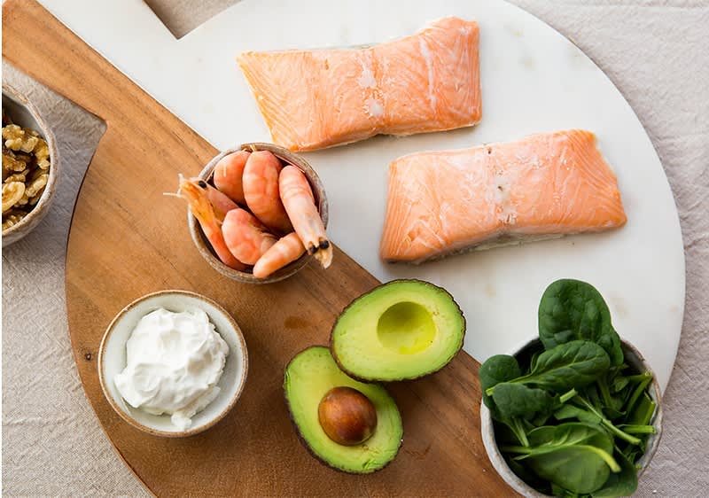 Gesunde Lebensmittel: Lachs, Garnelen, Avocado, Spinat, Walnüsse, Joghurt auf Holzbrett