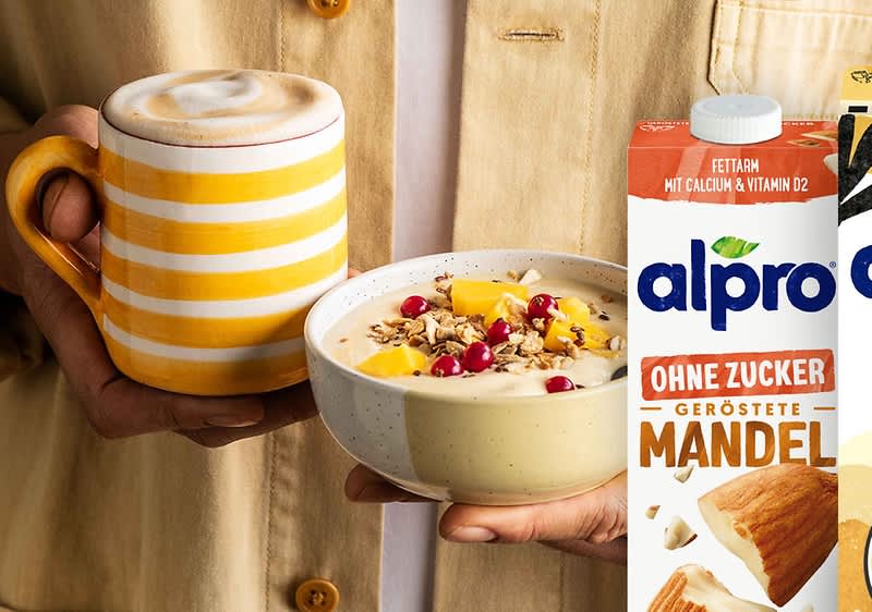 Frühstück mit Kaffee und Müsli neben Alpro Mandelmilch Verpackung