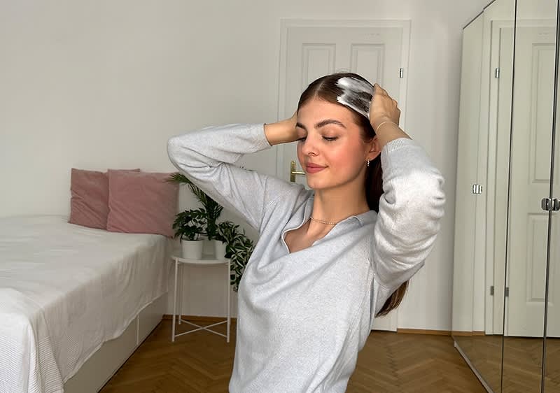 Frau gibt Schaumfestiger in ihre Haare in modernem Schlafzimmer mit Pflanzen und Spiegeln