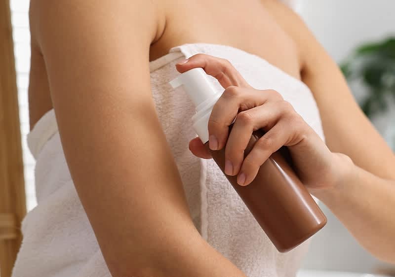 Selbstbräuner auftragen auf Arm einer Frau in weißem Handtuch