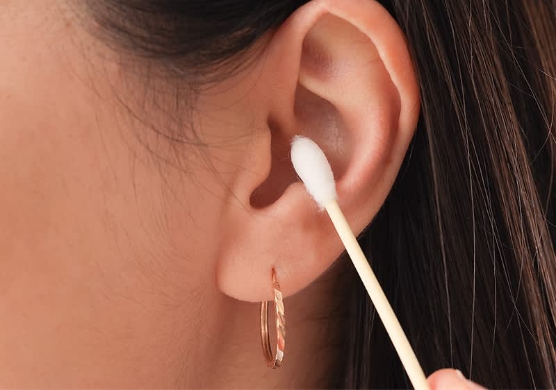 Ohrreinigung mit Wattestäbchen und Ohrring am Ohr