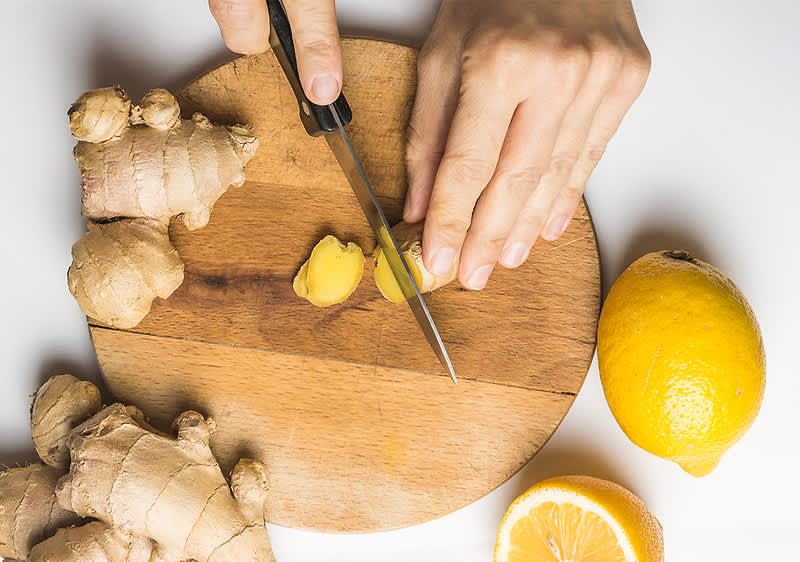 Ingwer und Zitrone auf Holzbrett mit Händen beim Schneiden