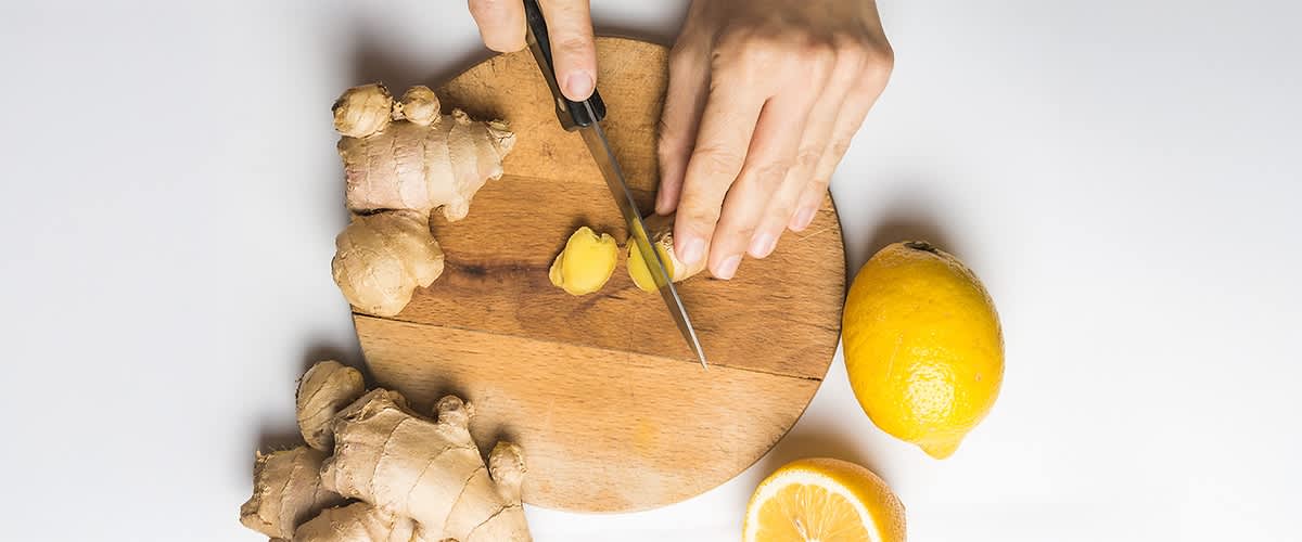 Ingwer und Zitrone auf Holzbrett mit Händen beim Schneiden