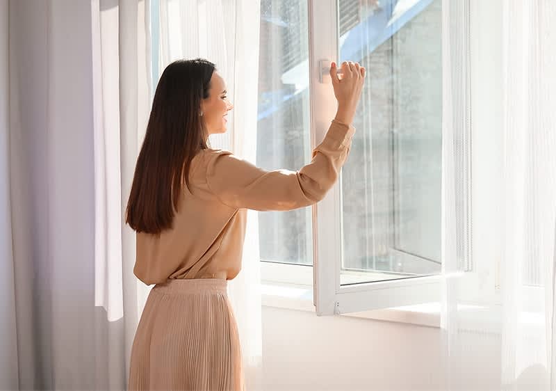 Frau am Fenster mit Vorhängen und Tageslicht